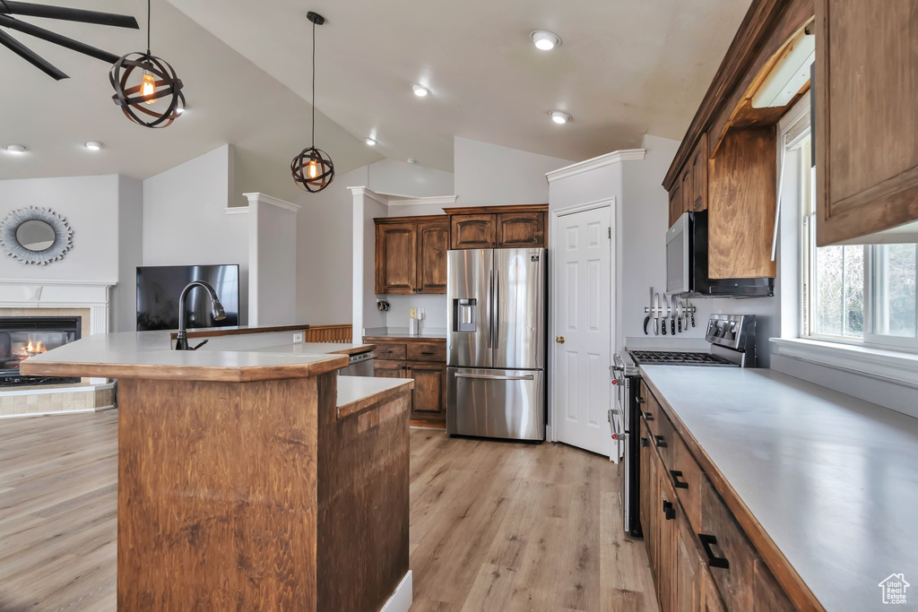 Kitchen with light hardwood / wood-style flooring, stainless steel appliances, vaulted ceiling, a center island with sink, and pendant lighting