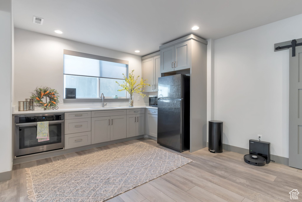 Kitchen featuring gray cabinetry, sink, stainless steel oven, light wood-type flooring, and black refrigerator