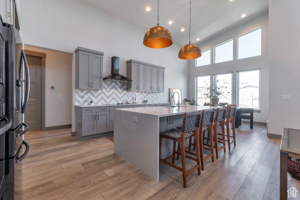 Kitchen with a towering ceiling, hanging light fixtures, tasteful backsplash, wall chimney range hood, and an island with sink
