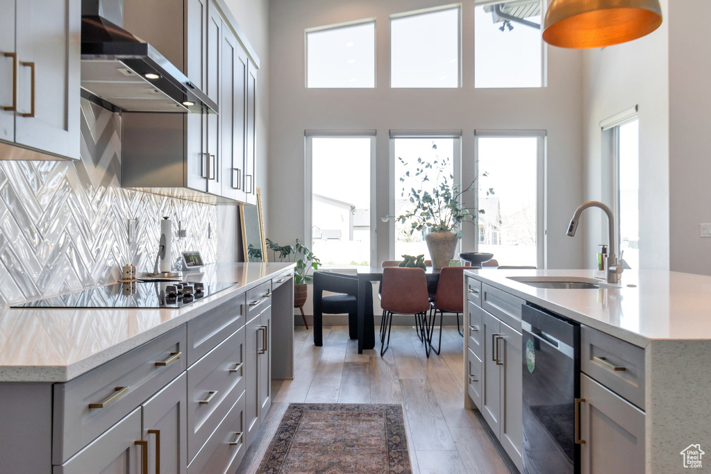 Kitchen featuring light hardwood / wood-style flooring, dishwasher, tasteful backsplash, wall chimney exhaust hood, and sink