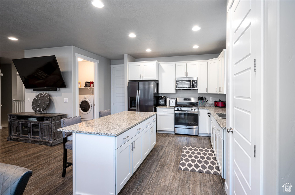 Kitchen featuring appliances with stainless steel finishes, white cabinetry, dark hardwood / wood-style floors, and washer / clothes dryer