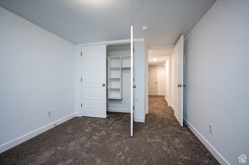 Unfurnished bedroom with a closet, dark carpet, and a textured ceiling