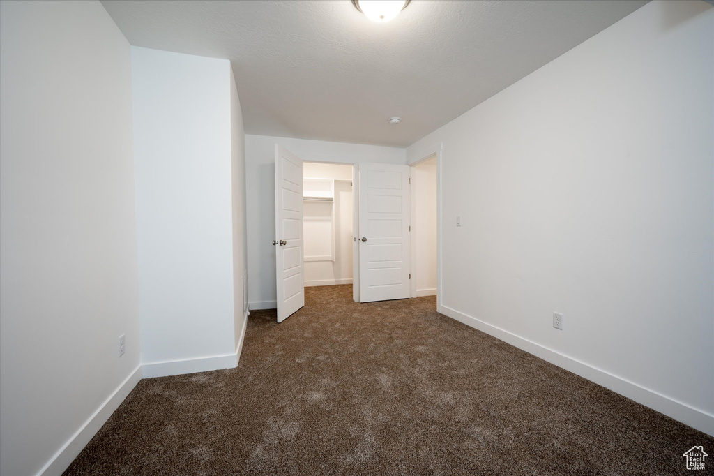 Unfurnished bedroom featuring a spacious closet and dark carpet