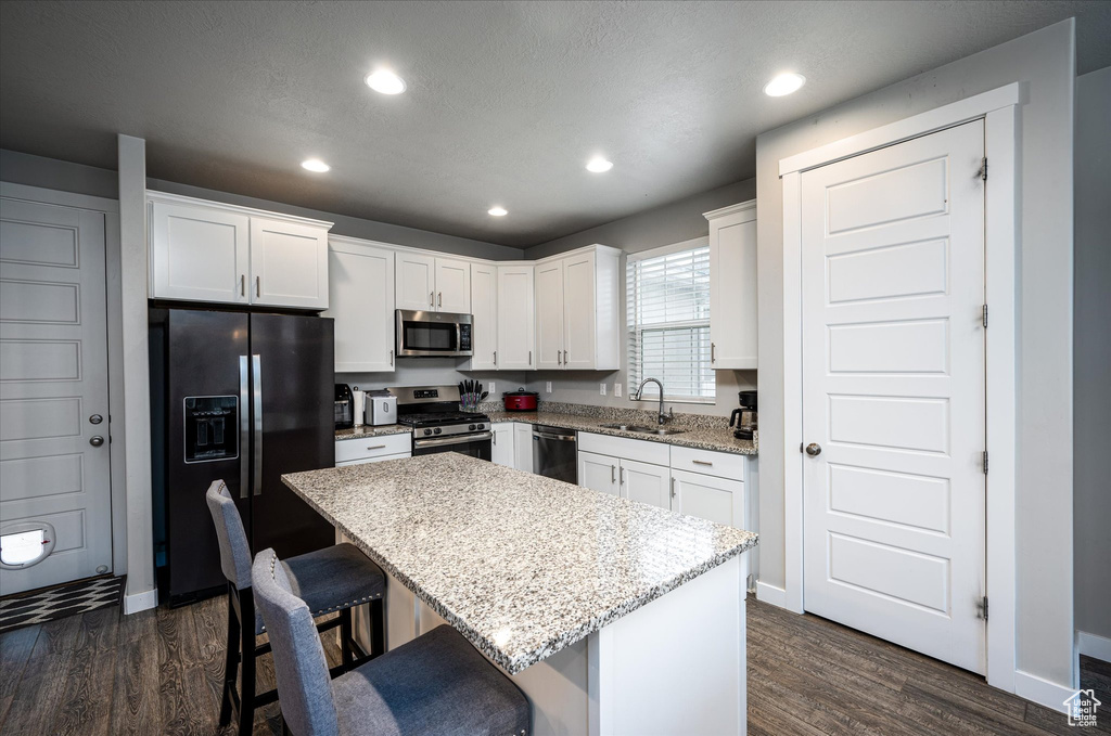 Kitchen featuring appliances with stainless steel finishes, a center island, white cabinets, dark hardwood / wood-style flooring, and a kitchen breakfast bar