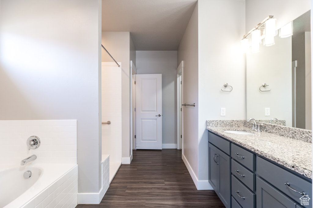 Bathroom featuring wood-type flooring, vanity, and tiled bath