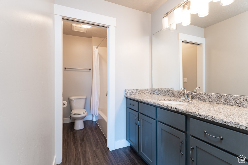 Full bathroom with vanity, toilet, shower / bath combo with shower curtain, and hardwood / wood-style floors