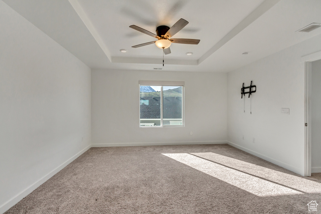 Carpeted spare room featuring ceiling fan and a raised ceiling