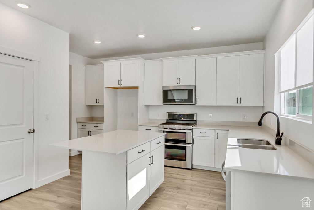 Kitchen with white cabinets, stainless steel appliances, a center island, and light wood-type flooring