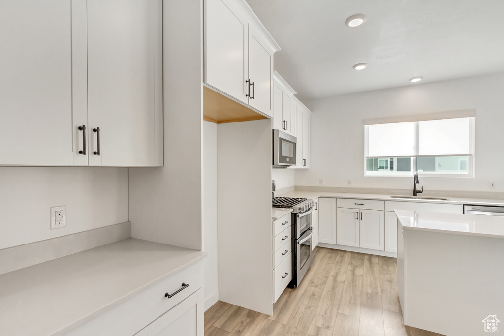 Kitchen featuring appliances with stainless steel finishes, light hardwood / wood-style floors, white cabinetry, and sink