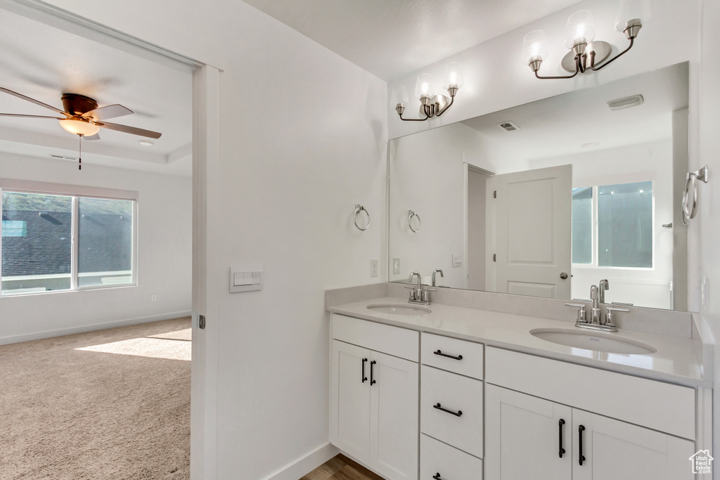 Bathroom with a wealth of natural light, dual bowl vanity, ceiling fan, and a raised ceiling