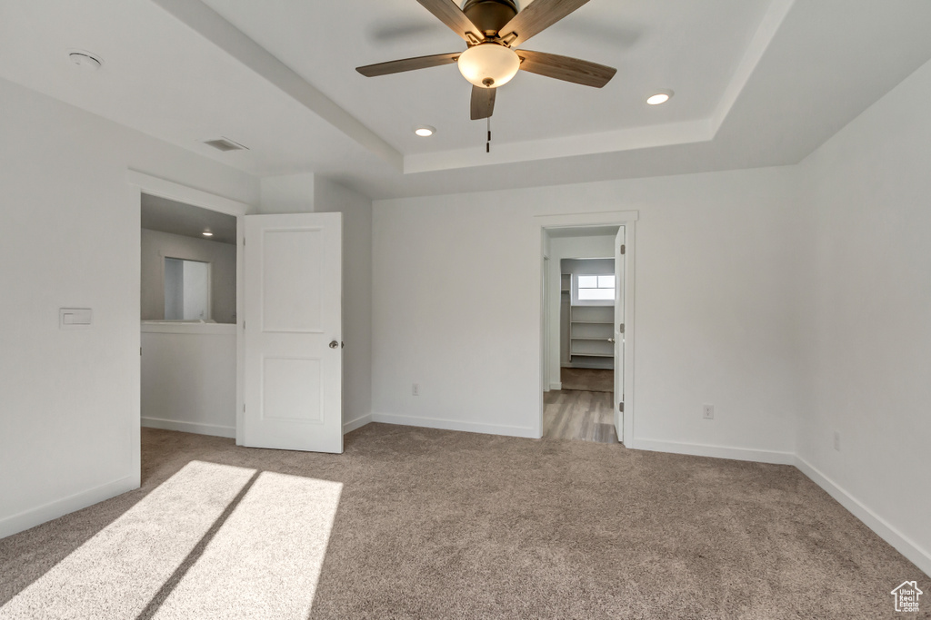 Unfurnished bedroom featuring a spacious closet, ceiling fan, light carpet, a closet, and a raised ceiling