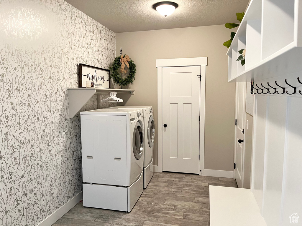 Clothes washing area with a textured ceiling, washer and clothes dryer, and light wood-type flooring