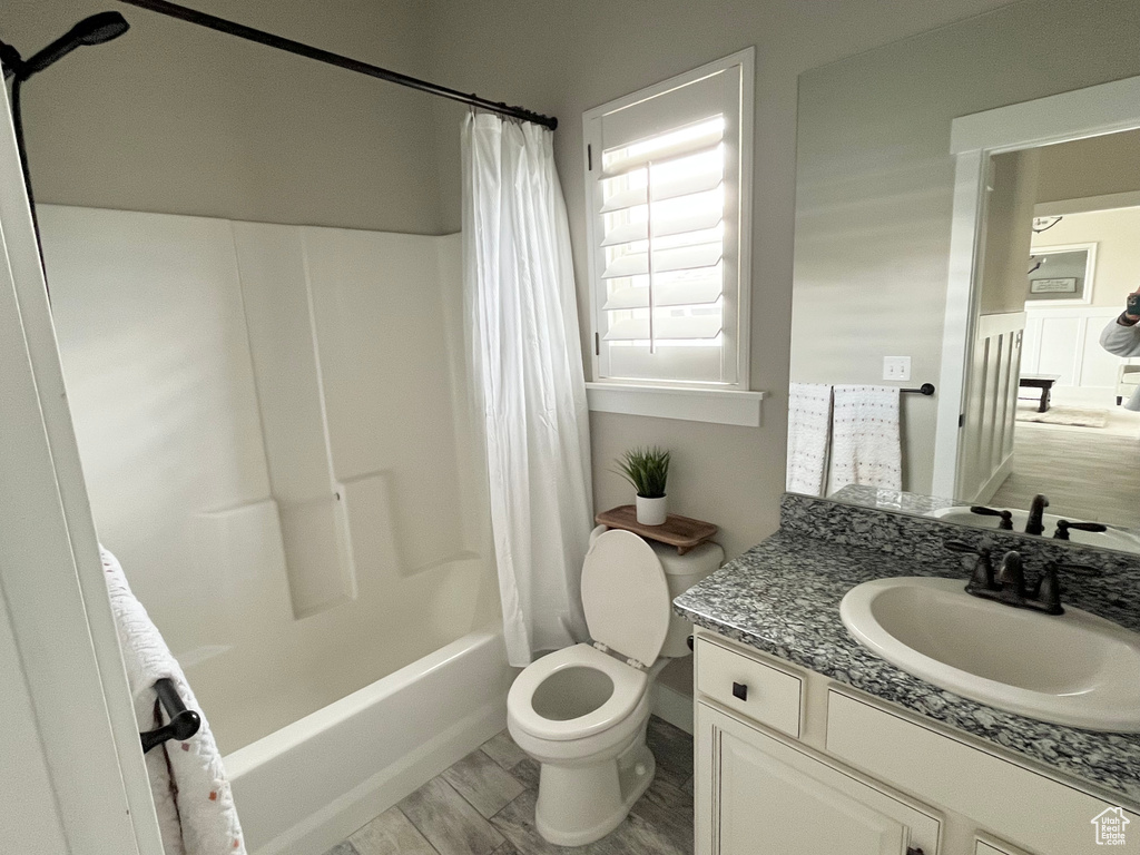 Full bathroom with shower / bathtub combination with curtain, hardwood / wood-style floors, toilet, and vanity with extensive cabinet space