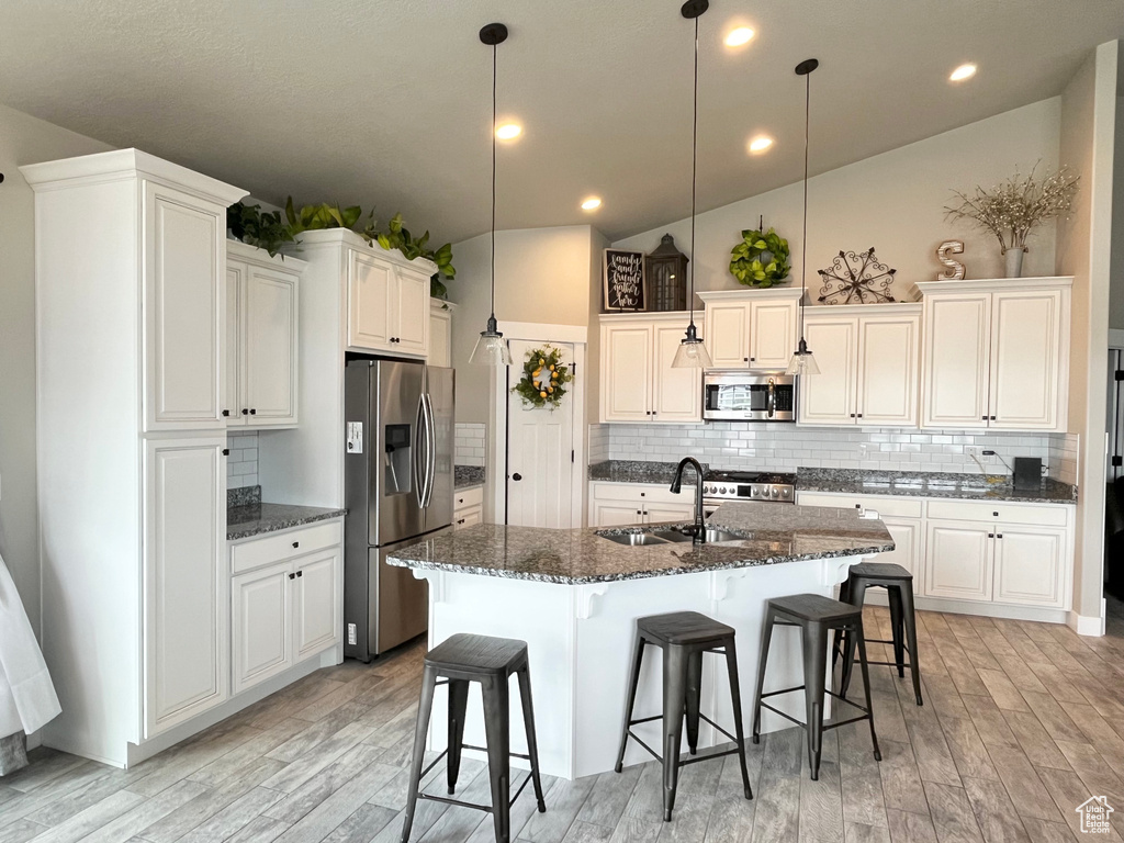 Kitchen featuring appliances with stainless steel finishes, decorative light fixtures, sink, and an island with sink