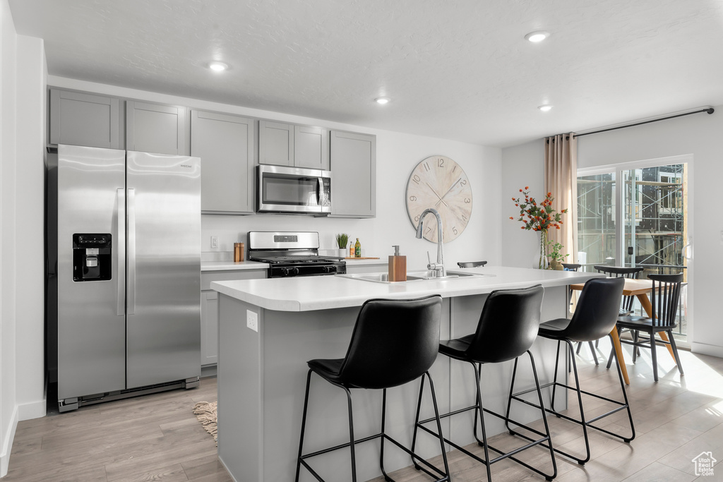 Kitchen featuring appliances with stainless steel finishes, light hardwood / wood-style floors, gray cabinetry, a breakfast bar area, and an island with sink