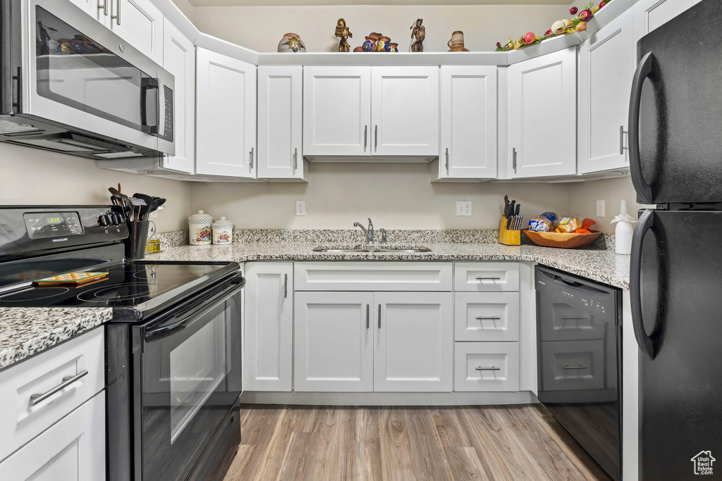Kitchen with light stone counters, white cabinets, sink, black appliances, and light hardwood / wood-style flooring