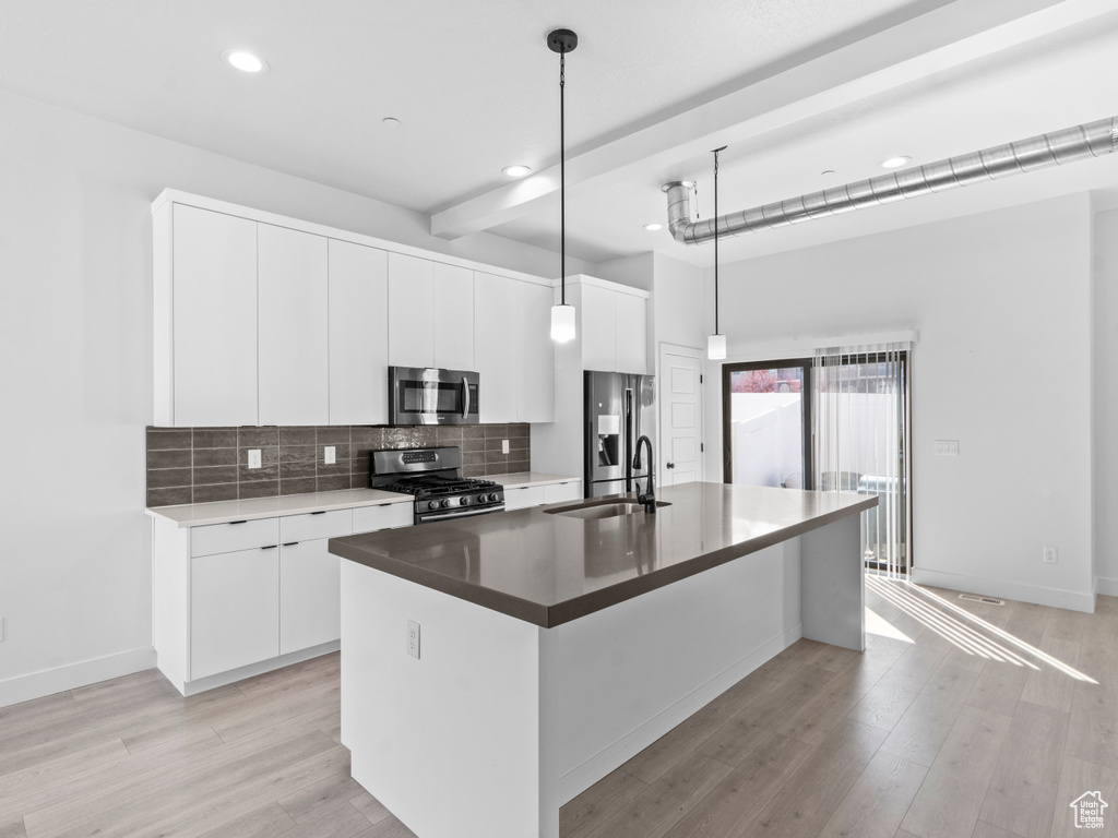 Kitchen featuring pendant lighting, white cabinets, stainless steel appliances, tasteful backsplash, and an island with sink