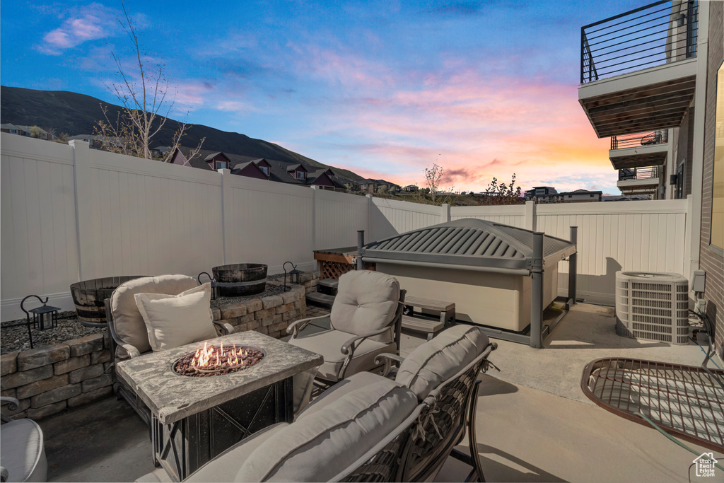 Patio terrace at dusk featuring central AC, a balcony, and an outdoor living space with a fire pit