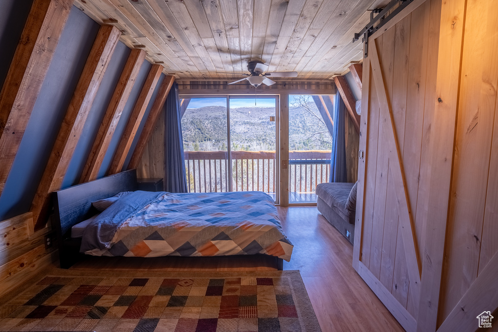 Unfurnished bedroom with a barn door, ceiling fan, access to outside, wooden ceiling, and a mountain view