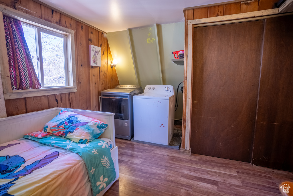 Bedroom with wooden walls, a closet, separate washer and dryer, and hardwood / wood-style flooring