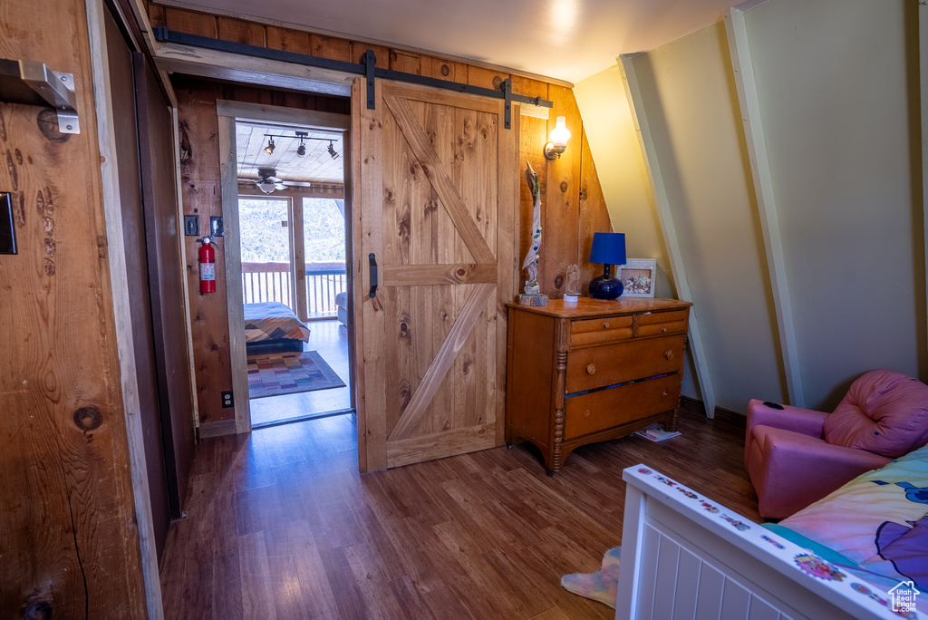 Bedroom featuring dark hardwood / wood-style floors, wooden walls, and a barn door