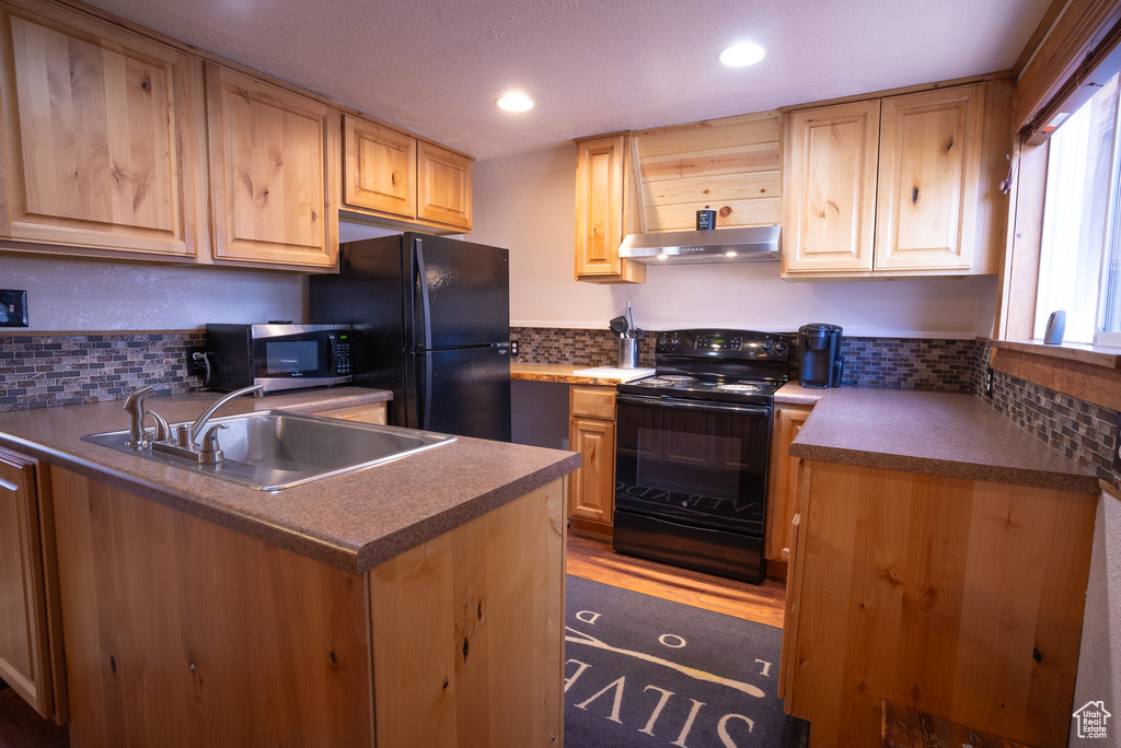 Kitchen with sink, backsplash, dark wood-type flooring, black appliances, and kitchen peninsula