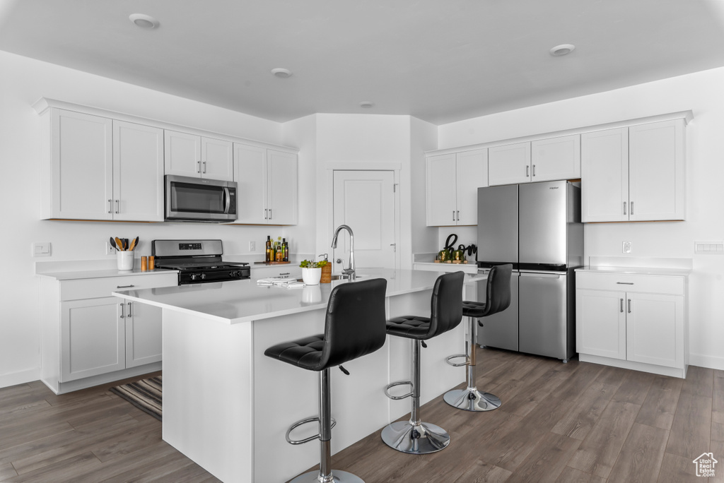 Kitchen with a kitchen breakfast bar, white cabinetry, stainless steel appliances, hardwood / wood-style flooring, and an island with sink