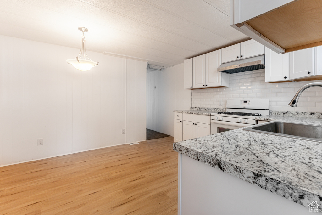 Kitchen with light wood-type flooring, backsplash, decorative light fixtures, white gas range, and sink