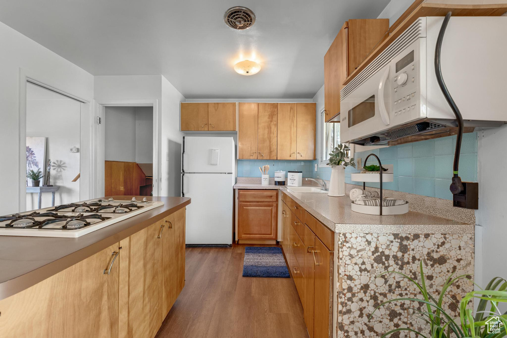 Kitchen with hardwood / wood-style floors, sink, white appliances, and tasteful backsplash