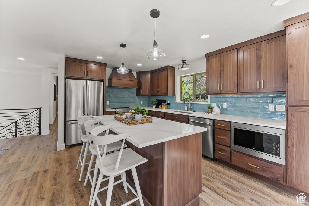 Kitchen with a kitchen island, backsplash, hanging light fixtures, stainless steel appliances, and light hardwood / wood-style flooring