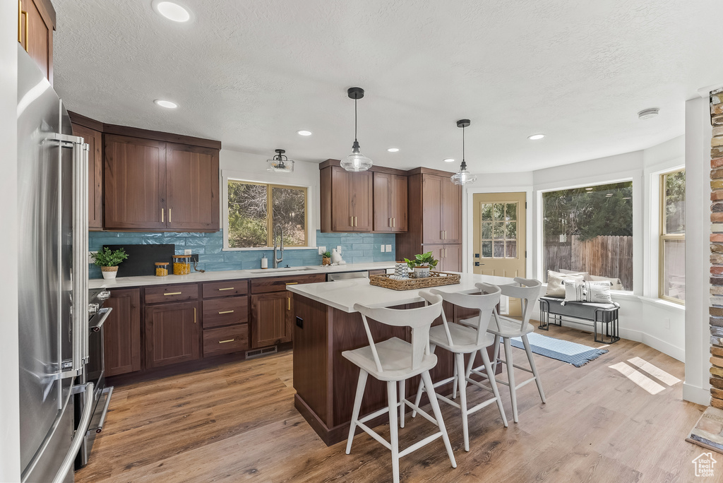 Kitchen featuring appliances with stainless steel finishes, a kitchen island, tasteful backsplash, light wood-type flooring, and decorative light fixtures