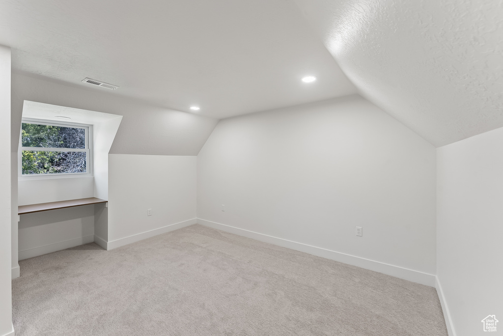 Additional living space featuring light colored carpet, lofted ceiling, and a textured ceiling