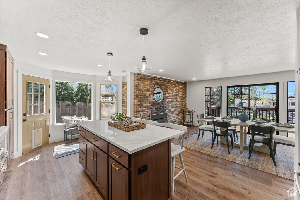 Kitchen with pendant lighting, light wood-type flooring, brick wall, a breakfast bar area, and a kitchen island