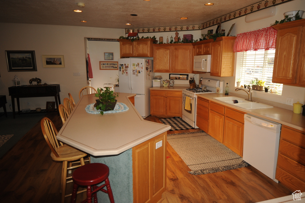 Kitchen with a kitchen island, a kitchen breakfast bar, white appliances, and sink