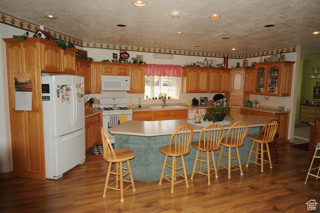 Kitchen featuring a kitchen island, a breakfast bar, dark wood-type flooring, and white appliances
