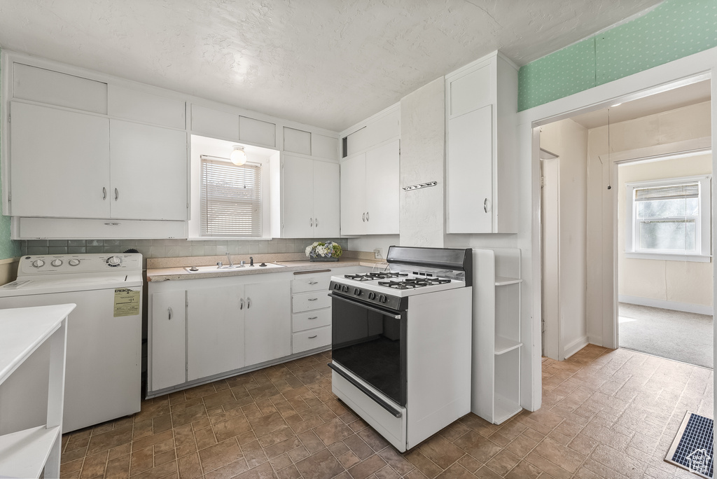 Kitchen featuring dark tile flooring, white range with gas cooktop, washer / clothes dryer, and white cabinetry