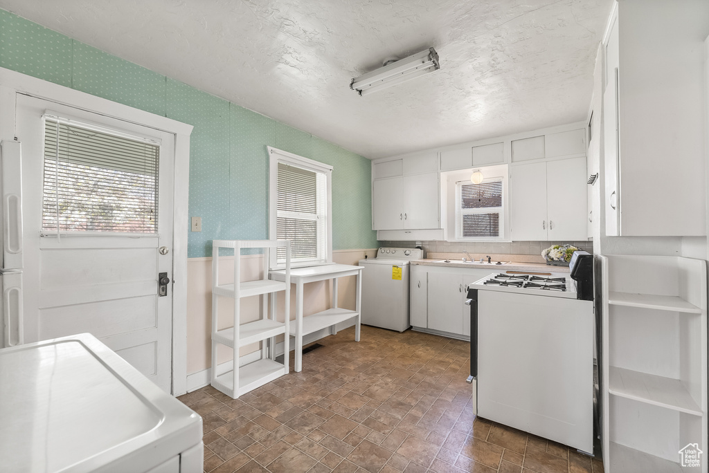 Kitchen with white cabinets, a wealth of natural light, washer / clothes dryer, and white appliances