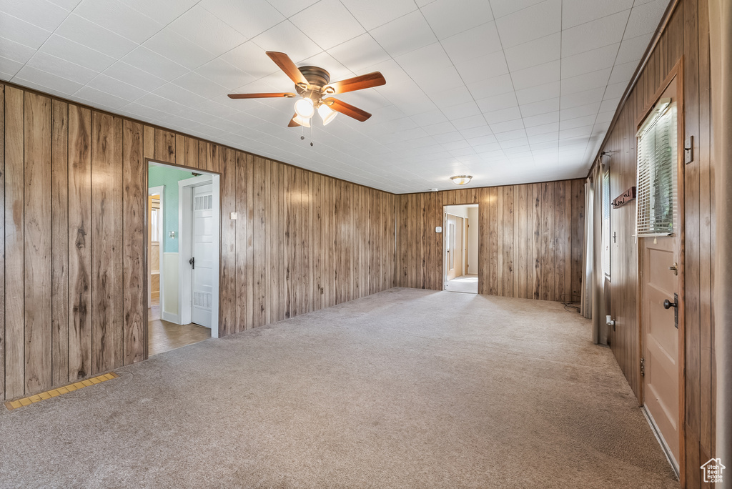 Carpeted spare room featuring ceiling fan and wood walls
