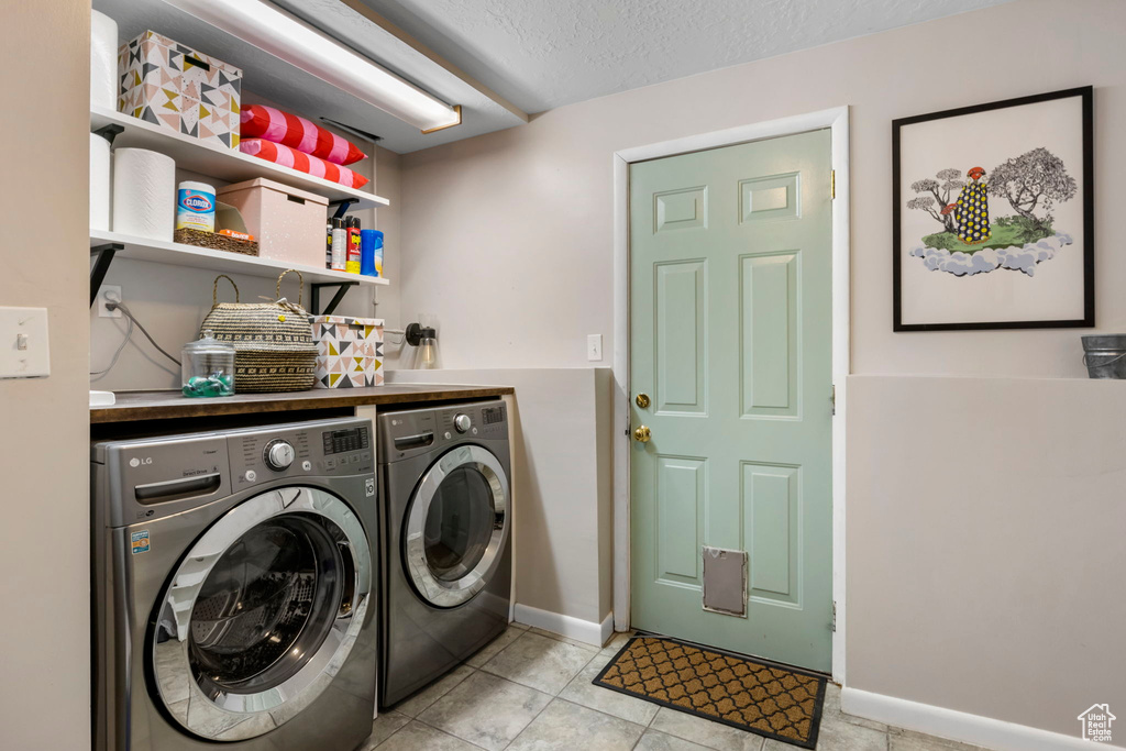 Clothes washing area with a textured ceiling, light tile floors, and washer and dryer