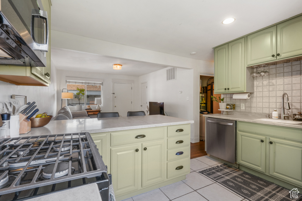 Kitchen featuring appliances with stainless steel finishes, light tile floors, green cabinetry, sink, and tasteful backsplash