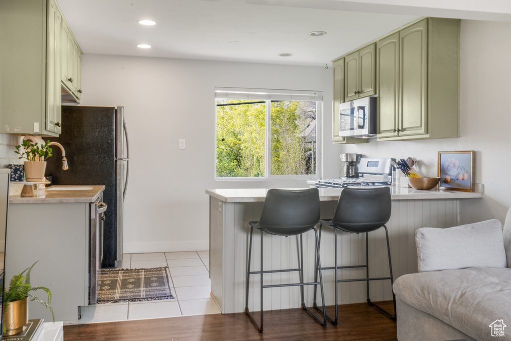 Kitchen featuring green cabinetry, kitchen peninsula, light tile floors, and a breakfast bar area