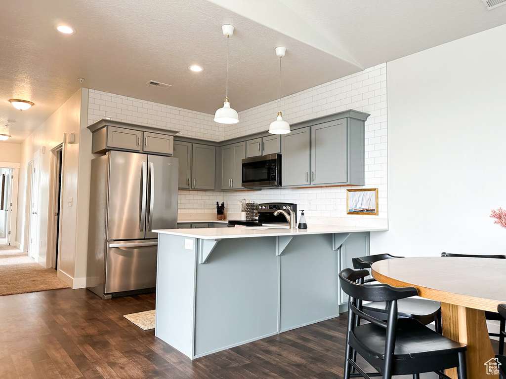 Kitchen featuring hanging light fixtures, a breakfast bar area, stainless steel appliances, tasteful backsplash, and dark wood-type flooring