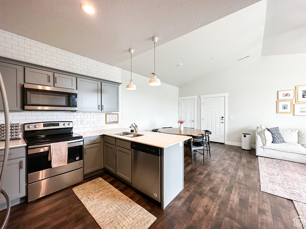 Kitchen featuring backsplash, dark hardwood / wood-style flooring, lofted ceiling, stainless steel appliances, and pendant lighting