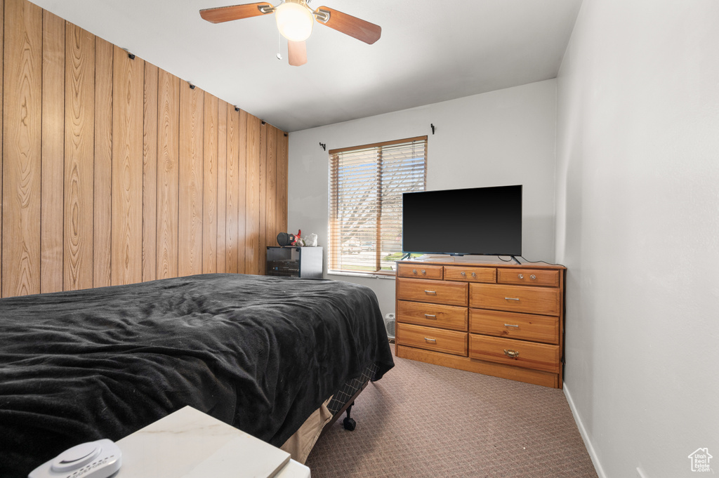 Carpeted bedroom with ceiling fan and wood walls