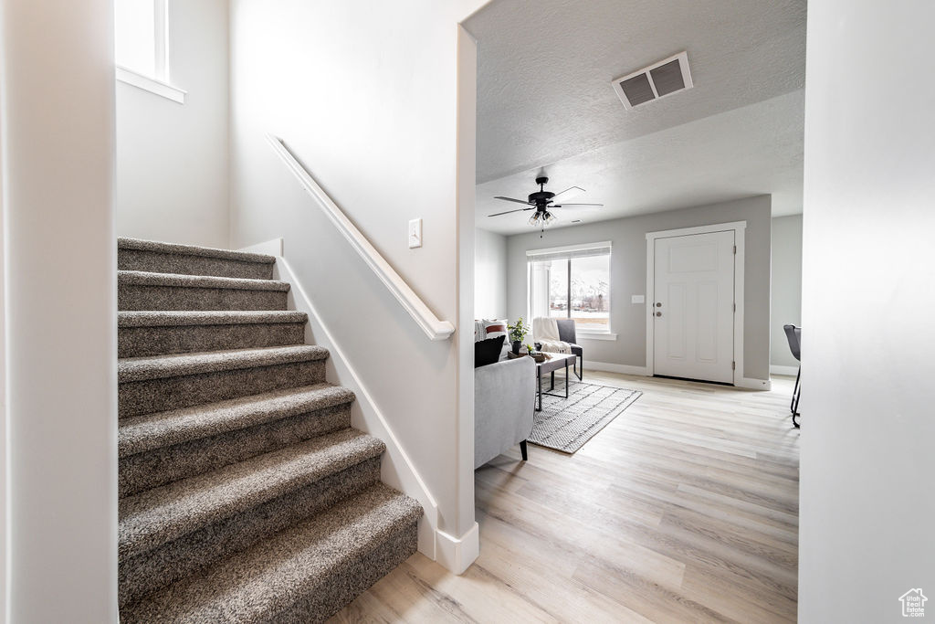 Stairway with a textured ceiling, ceiling fan, and light hardwood / wood-style floors