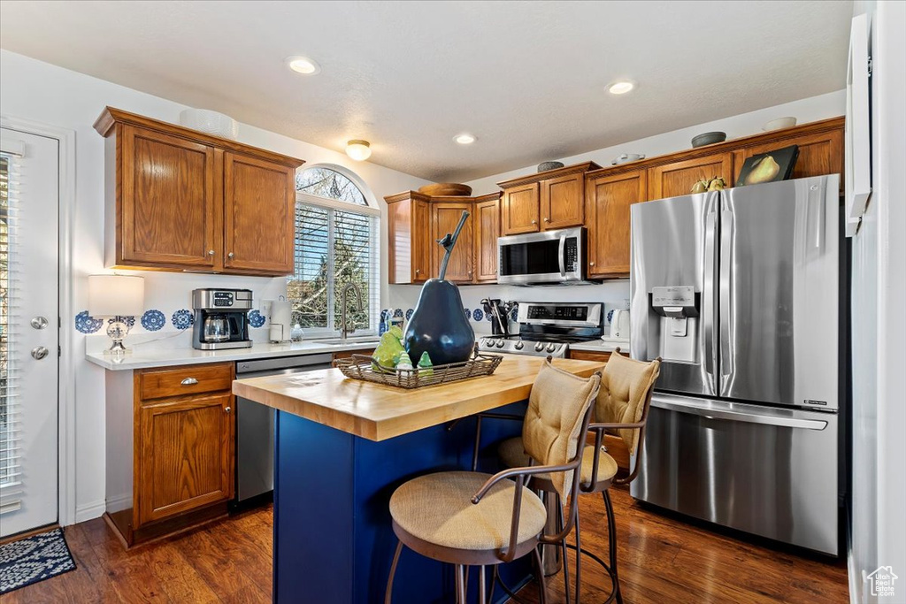 Kitchen with a center island, sink, stainless steel appliances, dark hardwood / wood-style floors, and a kitchen breakfast bar
