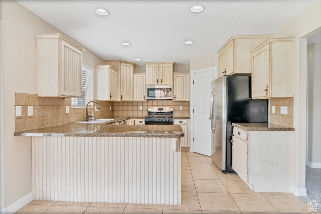 Kitchen with kitchen peninsula, appliances with stainless steel finishes, backsplash, sink, and light tile floors