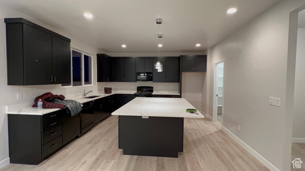Kitchen with decorative light fixtures, light hardwood / wood-style flooring, a center island, and black appliances