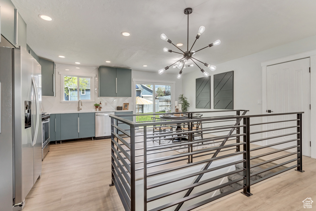 Kitchen featuring appliances with stainless steel finishes, light hardwood / wood-style flooring, hanging light fixtures, tasteful backsplash, and an inviting chandelier