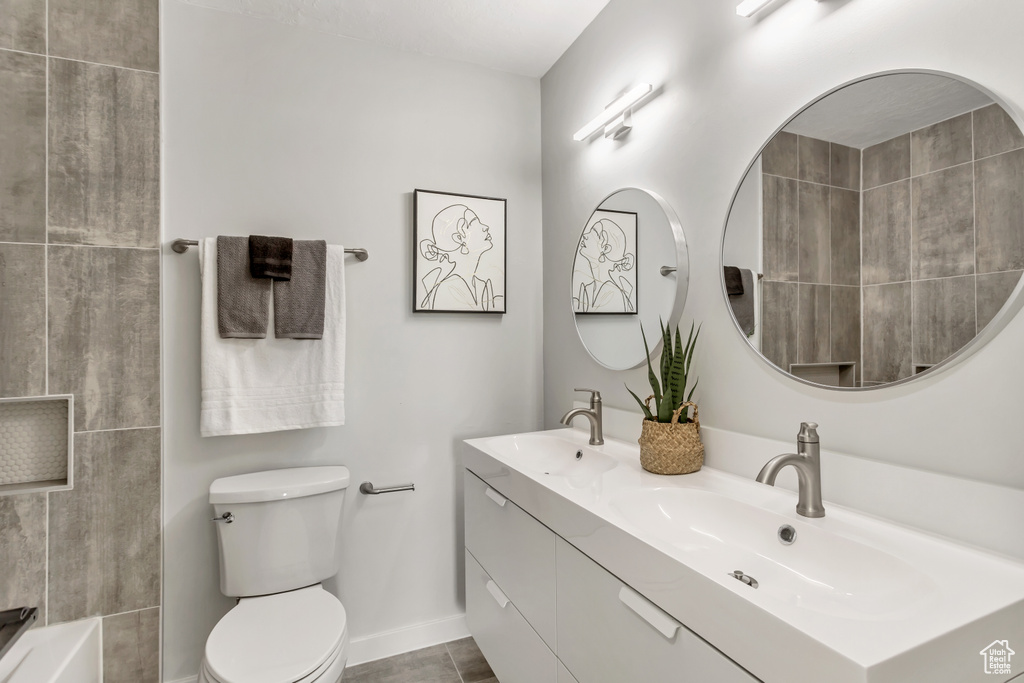 Bathroom featuring tile floors, toilet, large vanity, and dual sinks